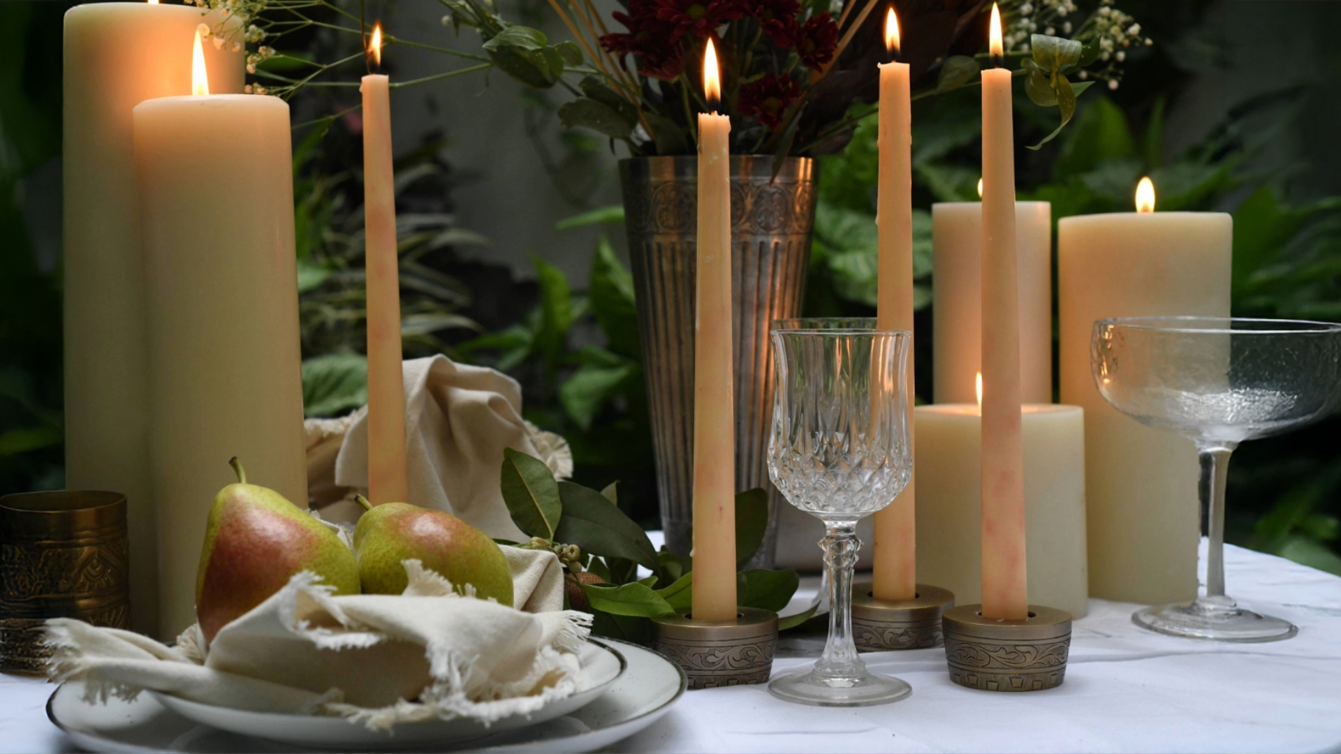 Candlelit table setting with apples, cake, and wine glasses on a white tablecloth.