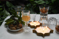 Candle holders with lit candles on a table with glasses and fruit bowl.